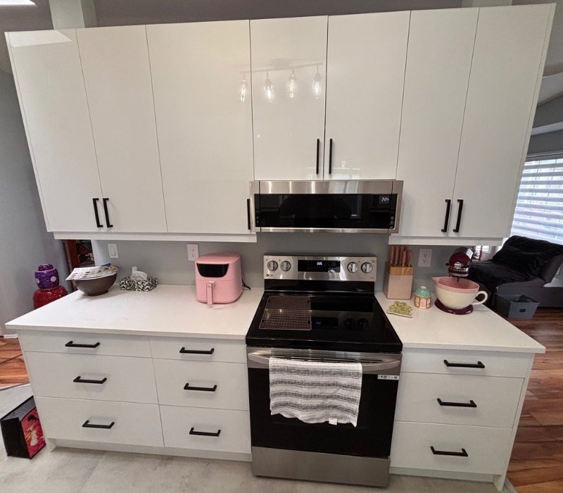 Kitchen remodeled with a white island and cabinets, central stainless stove with oven, microwave above, pendant lights overhead.